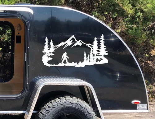 Bigfoot Sasquatch walking through mountain forest scene with evergreen pine trees and rugged peaks vinyl decal for RV camper and travel trailer