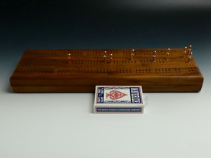 Walnut 3 Player Cribbage board with pegs in some holes and a deck of cards in front of the board.