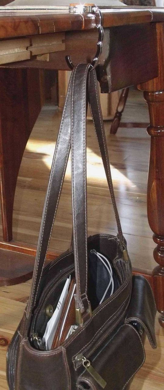 A purse hook with a purse hanging off the edge of a table.