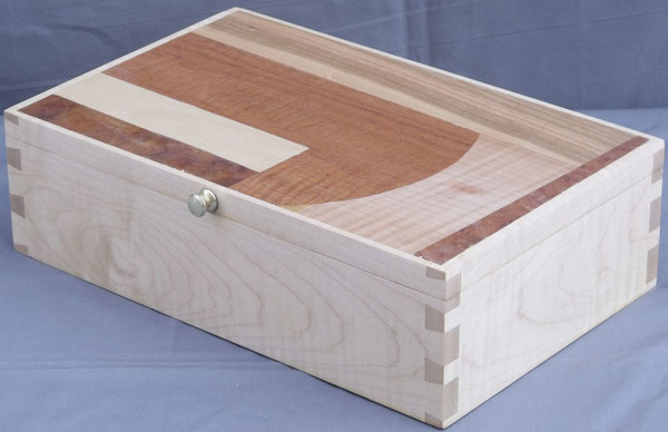 A handcrafted valet box made from light-toned solid curly maple wood, showcasing beautiful rippled grain patterns on the sides and prominent, dark through-dovetail joinery on the corner edges.