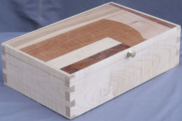 A handcrafted valet box made from light-toned solid curly maple wood, showcasing beautiful rippled grain patterns on the sides and prominent, dark through-dovetail joinery on the corner edges.