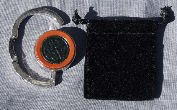 A purse hook that is partially open next to the black velveteen bag that comes with it.