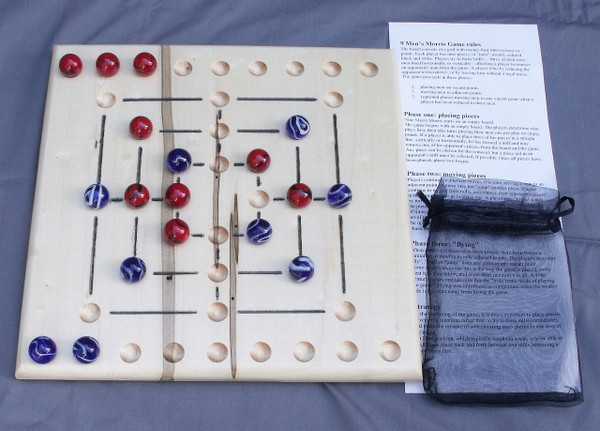 A Nine Man Morris board in the middle of a game with marbles on the playing field, the instructions, and the storage bag.