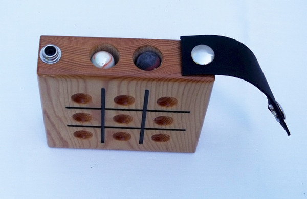A top-down view  of the Tic Tac Toe game with the leather strap unsnapped on one side showing the marbles in the storage compartment.