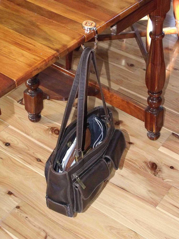 A purse hook with a purse hanging off the edge of a table.