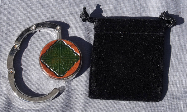 A purse hook that is partially open next to the black velveteen bag that comes with it.