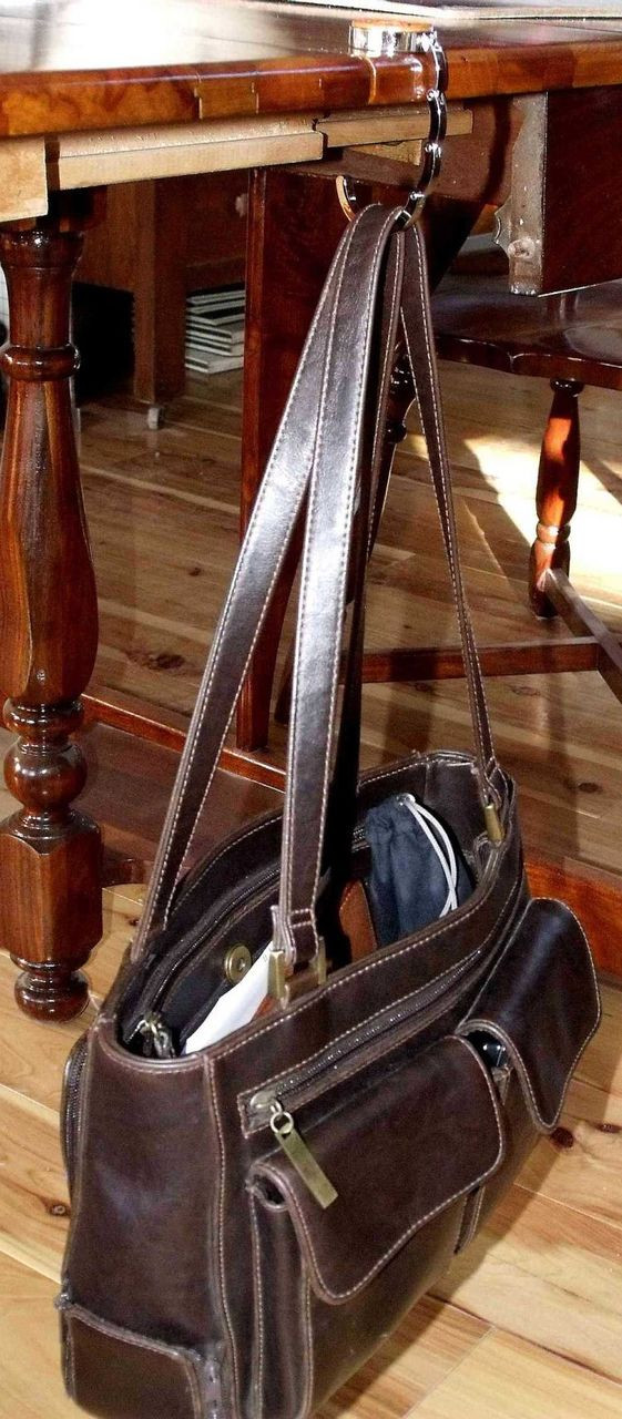A purse hook with a purse hanging off the edge of a table.