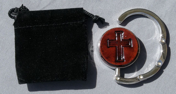 A purse hook that is partially open next to the black velveteen bag that comes with it.