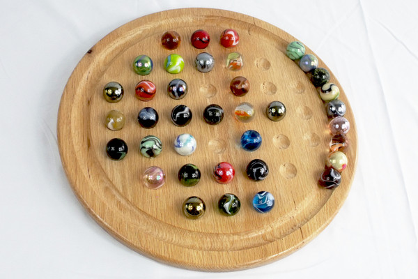 The Boulder sized Marble Solitaire game during game play with some marbles on the board and some in the outer ring.