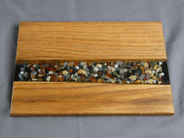 Oak Small River Pour Charcuterie Serving Board #20
This charcuterie serving board is made from solid oak. Small stones and epoxy resin were added to the center to create a river pour effect.  

The charcuterie board is about 7 1/2" wide, 12" long, and 5/8" thick. 

It is finished with food safe cutting board oil and protective cutting board wax.