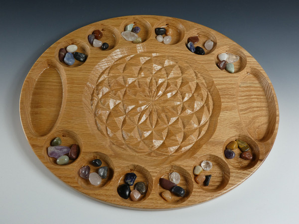 The large deluxe mancala board in oak with the flower of life in the center and beautiful stones in their starting positions.