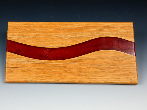 The other side of the an oak serving board with red epoxy resin flowing through it.  The red epoxy has mica powder which gives is a subtle swirl look.