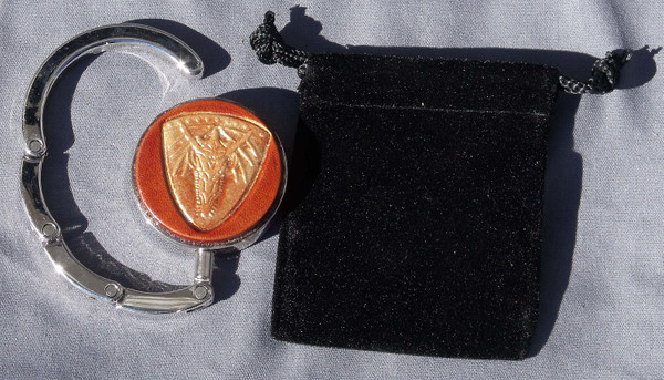 A purse hook that is partially open next to the black velveteen bag that comes with it.