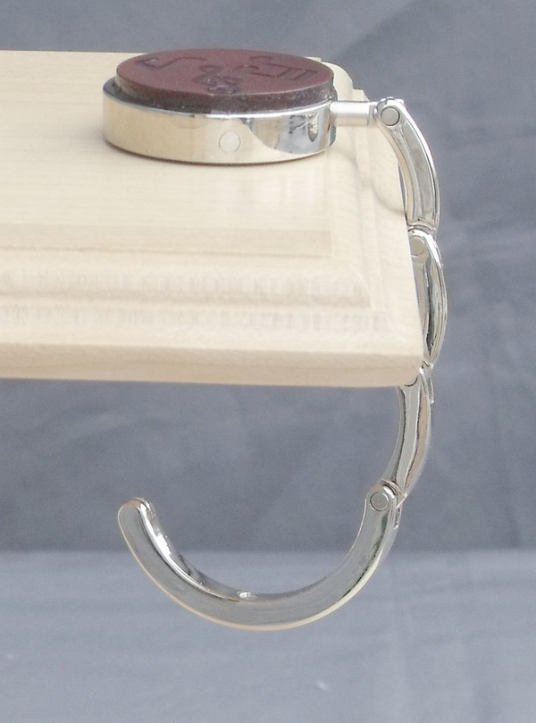 Side view of an open purse hook hanging off the edge of a table.