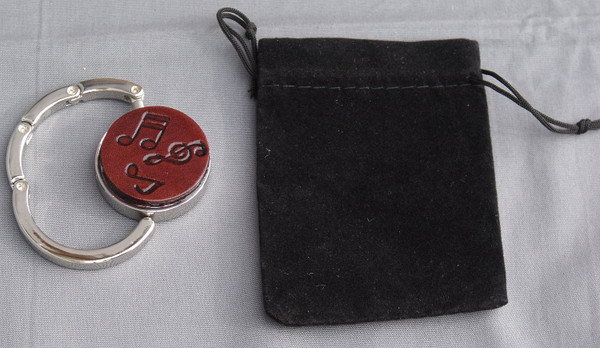 A purse hook that is partially open next to the black velveteen bag that comes with it.