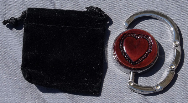 A purse hook that is partially open next to the black velveteen bag that comes with it.