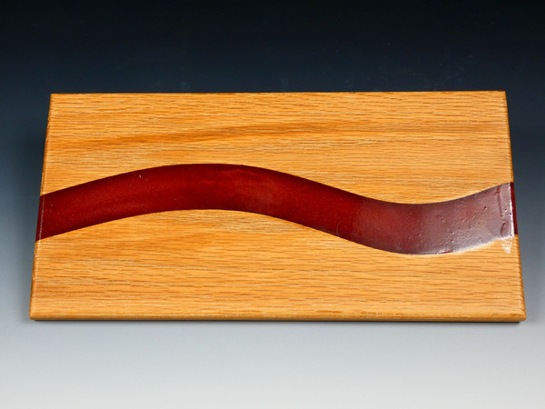 The top of the oak serving board with red epoxy resin flowing through it.  The red epoxy has mica powder which gives is a subtle swirl look.