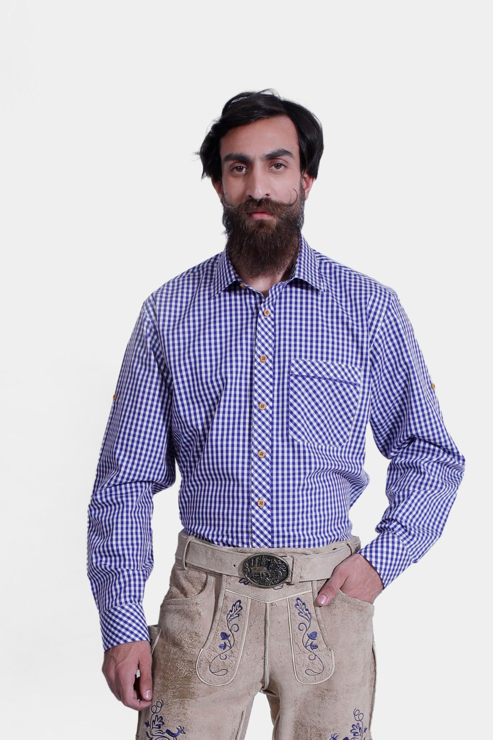 A man wearing the Bach Lederhosen Shirt, a blue and white checkered long-sleeve shirt with a front pocket. He pairs it with light brown leather Lederhosen adorned with blue embroidery and a decorative belt buckle. This traditional Bavarian outfit is perfe