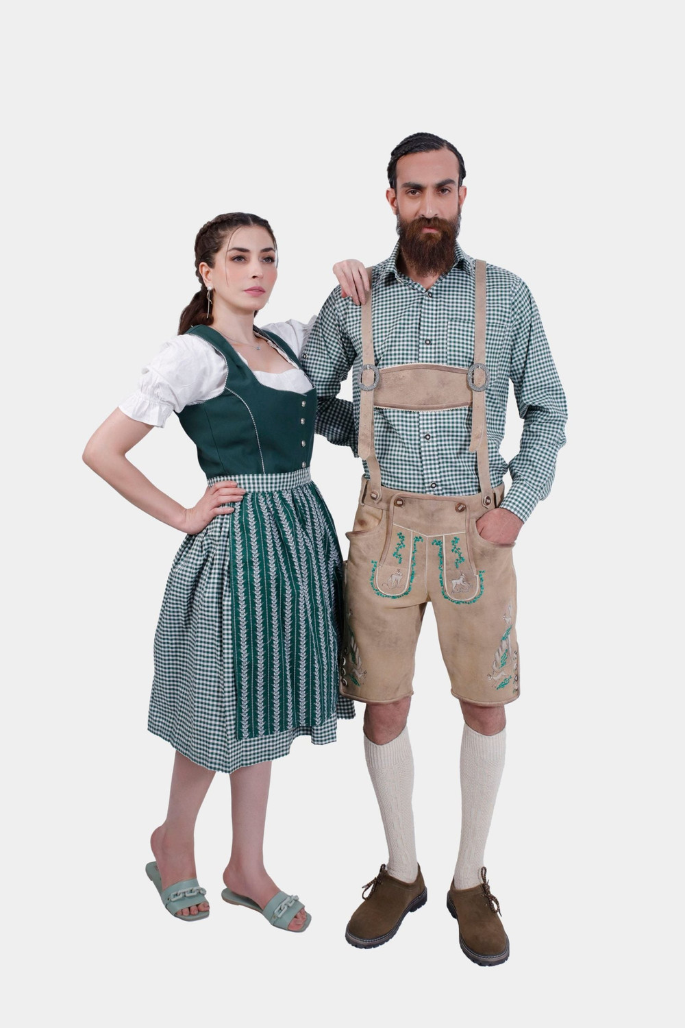 A man and woman in traditional Bavarian attire. The woman is wearing a green dirndl dress with a white blouse, while the man is dressed in beige lederhosen with green embroidery and a green checkered shirt. Both stand confidently, showcasing their stylish