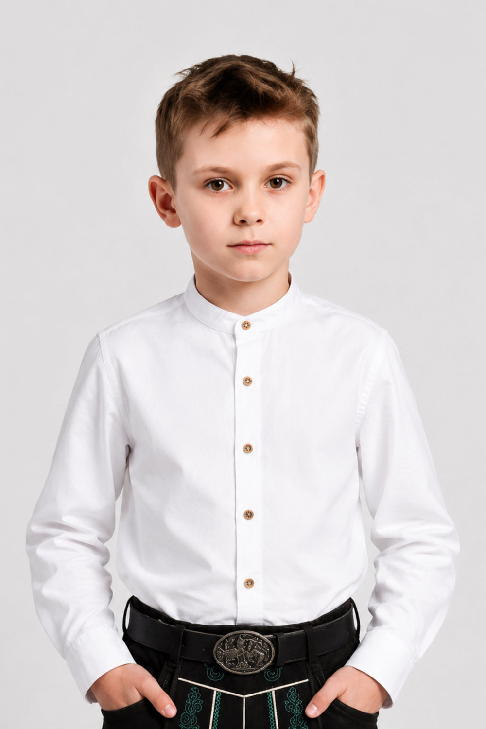 Boy wearing Elias kids white cotton shirt paired with traditional black lederhosen shorts in studio portrait