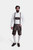 A man with a beard stands against a white background, wearing the "Angry Stag Eibsee Lederhosen." These traditional dark brown Lederhosen are knee-length and feature intricate light-colored embroidery on the bib, side panels, and around the leg openings. 