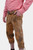 Another side view of a man in traditional Bavarian clothing. The focus is on the brown leather Bundhosen with intricate embroidery, paired with a red and white checkered shirt. The man stands with his hand in his pocket, emphasizing the authentic craftsma