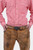 Close-up of a man wearing a red and white checkered shirt tucked into brown leather Bundhosen. The focus is on the intricate detailing of the belt buckle and the texture of the leather pants. The man's hands are in his pockets, and the shirt has wooden bu