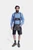 A man wearing traditional Bavarian Lederhosen. He is dressed in a blue checkered long-sleeve shirt paired with black leather shorts featuring intricate white embroidery and suspenders. The look is completed with dark green knee-high socks and brown shoes,