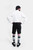 Rear view of a man in a white shirt and black lederhosen with hands on hips, showing gray and green socks, against a white background.