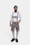 A man wearing traditional Bavarian Lederhosen. He is dressed in a white dress shirt with a black bow tie and light gray leather shorts adorned with intricate black embroidery and suspenders. He completes the outfit with light gray knee-high socks and blac