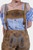 Close-up of the Clara Schumann Lederhosen showing the detailed blue embroidery on the bib, paired with a blue and white checkered blouse. The image highlights the quality and design of the Lederhosen.
