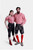 A couple dressed in matching Bamberger Couple Outfits. The woman is wearing a red checkered off-shoulder blouse paired with elegant black knee-length lederhosen adorned with white embroidery and stylish red ankle boots. The man is wearing a red checkered 