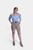 Full-body view of a woman in a blue checkered blouse and beige Lederhosen shorts, posing with her hands on hips.