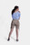 Rear view of a woman wearing beige Lederhosen shorts and a blue checkered blouse, with her hair tied back, showcasing the back details of the outfit.