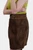 A Side view of the brown leather skirt, highlighting its detailed stitching and the ornate circular buckle on the belt. The woman's arm is partially visible, crossed over her body, emphasizing the texture and fit of the skirt.