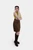 Slightly turned a body, view of the woman in the lime green top and brown leather skirt. She is also wearing knee-high brown boots, with one hand on her hip and the other resting by her side, posing confidently against a plain white background.
