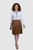 Woman wearing a brown traditional Bavarian leather skirt with embroidery and a white blouse on a plain background.