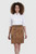 Woman wearing a white shirt and brown leather skirt on a light gray background