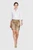 A woman wearing a white embroidered button-down shirt with three-quarter sleeves, paired with beige Lederhosen shorts featuring intricate embroidery and decorative buttons. She is wearing beige high heels and walking confidently.