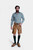 man wearing a traditional Lars Eidinger Lederhosen outfit, featuring tan leather shorts with green embroidery, a green checkered shirt, and green knit socks, standing with a neutral expression.