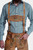 A man wearing a Lars Eidinger Lederhosen outfit, including tan leather shorts with green embroidery, a green checkered shirt, and traditional leather suspenders, standing with hands in pockets.