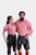 A couple dressed in matching Bamberger Couple Outfits. The woman is wearing a red checkered off-shoulder blouse paired with elegant black knee-length lederhosen adorned with white embroidery and stylish red ankle boots. The man is wearing a red checkered 