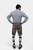 A man with a beard is standing with his back to the camera, hands on hips, wearing a grey and white checkered shirt and grey leather lederhosen. He is also wearing green and grey knee-high socks and brown shoes. The lederhosen has pockets on both sides an