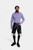 A man with a beard is standing against a white background, wearing a purple and white checkered shirt paired with black lederhosen decorated with green embroidery. He has his right hand in the pocket of the lederhosen, and is also wearing dark green knee-