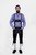 A man with a beard and styled hair wearing a blue and white checkered shirt and black leather bundhosen with suspenders, standing with his hands in his pockets and looking directly at the camera, highlighting the intricate embroidery and buckle details.