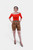 Full-body front view of a woman modeling Queen Victoria Lederhosen, showcasing knee-length shorts with natural-tone embroidery and a red off-shoulder top. damen lederhose kurz​, kurze lederhose damen​