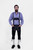 A man with a beard is wearing a blue checkered shirt and Marx Bundhosen with suspenders. The suspenders have decorative buckles and are attached to the pants, which feature intricate front embroidery. The man stands with both hands in his pockets, wearing black shoes and socks.