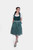 Full-length view of a woman standing in Dirndl Sukowa, styled with a green bodice, patterned skirt, and a gingham apron, complemented by green sandals. 
Grünes Dirndl