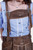 Close-up of a woman wearing blue and white checkered blouse and brown lederhosen with intricate embroidery and metal buckles on the bib.