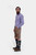 Side profile of the man in the blue checkered shirt and brown DanubeLederhosen, with his left hand in his pocket, standing against a white background.